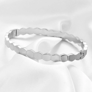 Macro shot of silver hexagonal honeycomb bangle with clasp on white silk fabric