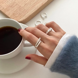 Close-up of 925 sterling silver twist ring and layered band on hand with coffee cup