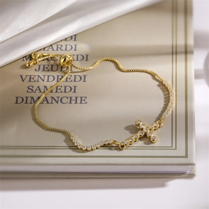Detail of gold cross bracelet with cubic zirconia on a box chain and slider clasp