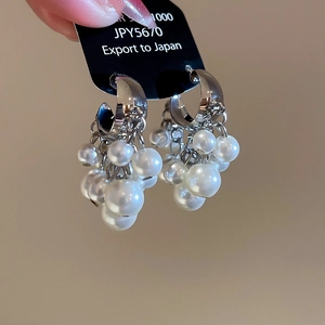 Macro view of C-shaped silver beaded tassel earrings featuring clusters of white pearls
