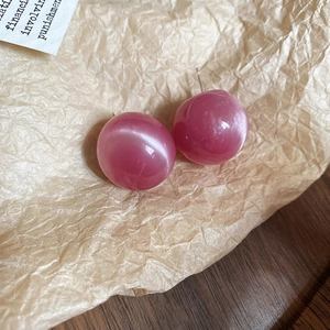 Macro shot of pink round cat-eye earrings on a textured beige paper background