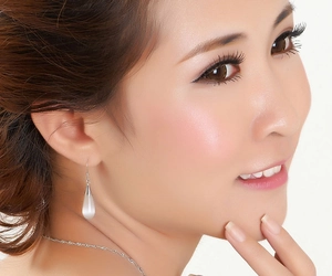 Close-up of a model wearing elegant white opal teardrop earrings and a silver chain necklace