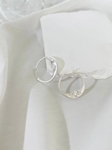 Artistic silver crescent moon face hoop earrings displayed on a white textured stone base