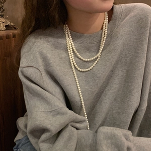 Classic multi-layer long pearl necklace displayed on a model wearing a grey sweatshirt