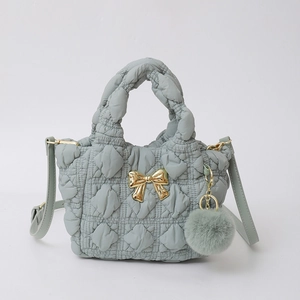 Détail du sac en nylon matelassé gris avec nœud doré et accessoire de pompon en peluche