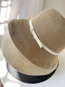 Close-up of three woven straw sun hats with elegant bows in beige, khaki, and black