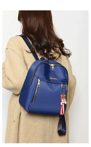 Detail view of dark blue Oxford backpack with gold zippers and a bear toy pendant