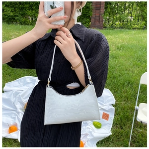 White crocodile pattern shoulder bag shown on grass backdrop with model in black dress