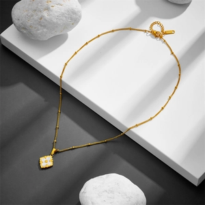 Golden titanium steel necklace with white shell clover pendant on a geometric stand