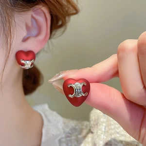 Close-up of red heart earrings featuring a matte finish and silver metal logo detail