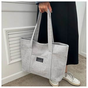 Detail of grey canvas tote bag with woven texture held by model in minimalist setting