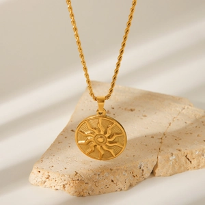 Close-up of golden sunburst pendant with twisted chain on a beige stone block