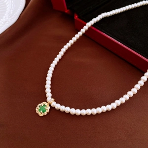 Close-up of pearl necklace with gold镂空 pendant and emerald-green gemstone detail