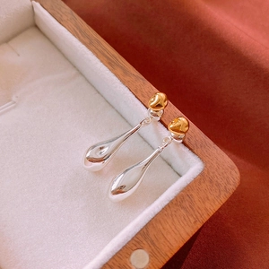 Macro detail of gold and silver waterdrop earrings in a white jewelry display box