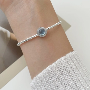 Close-up of silver beaded bracelet featuring a round blue gemstone with diamond halo