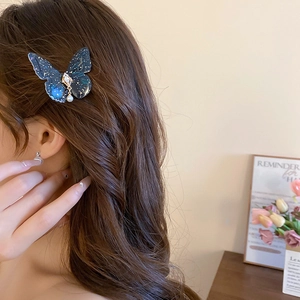 Détail d'une pince à cheveux papillon bleue avec strass et perle sur des cheveux bruns