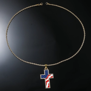 Détail d'un pendentif croix dorée avec motif drapeau USA et strass sur fond noir brillant