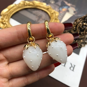 Macro detail of French style strawberry earrings with pearl accents and gold hoops