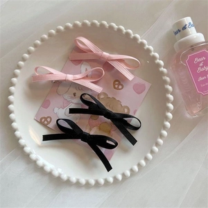 Pink and black ribbon bow hair clips set on a decorative white porcelain tray