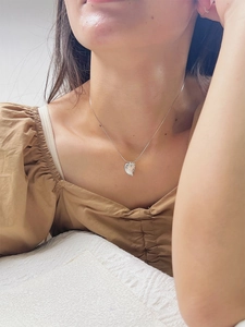 Close-up of heart-shaped shell pendant on a fine silver chain worn by a model