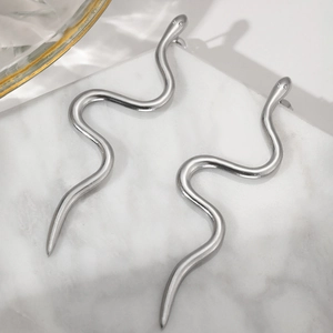 Macro shot of silver minimalist wave snake earrings on a white marble display base