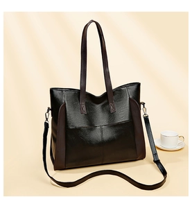 Detail view of large black faux leather tote bag with brown handles on a warm background