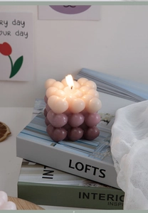 Close-up of lit gradient bubble cube candle in pink and mauve on decorative books