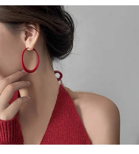 Close-up of a large red matte round hoop earring worn by a model in a red knit top