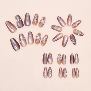 Dettaglio di unghie finte effetto cat eye con farfalle, perle e strass luccicanti