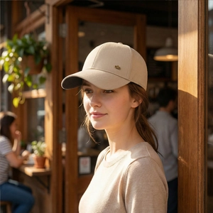 Classic beige cotton baseball cap with a circular metal logo shown in an outdoor cafe setting
