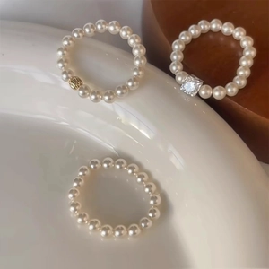 Detailed shot of elastic pearl rings with gold accents and crystals on a white plate