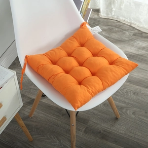 Detail of orange square quilted chair cushion with textured fabric on a white Nordic chair