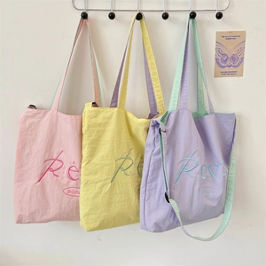 Three macaron-colored canvas tote bags in pink, yellow, and purple hanging on a wall