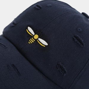 Close-up of navy blue cotton baseball cap with bee embroidery and distressed ripped details