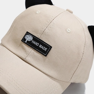 Close-up of beige cotton baseball cap with cute black plush cat ears and woven label