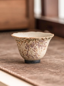 Detail of hand-painted wisteria ceramic teacup with gold-trimmed edges on a textured mat