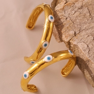 Golden titanium steel cuff bracelet with blue evil eye charms on a natural rock surface