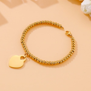 Close-up of 18k gold-plated beaded bracelet with smooth heart charm on warm background