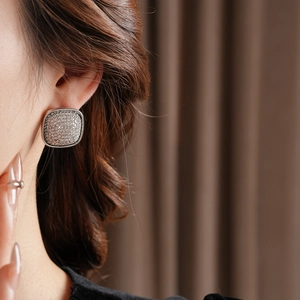 Close-up of a silver cushion-shaped earring with pavé stones worn by a model