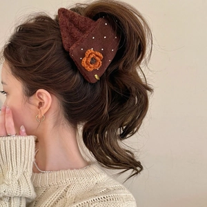Détail d'une pince à cheveux fleurie en tricot portée sur une queue de cheval avec pull