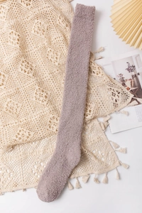 Detail of plush coral fleece over-knee sock in purple gray on lace fabric background
