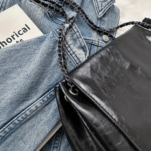 Minimalist black oil leather shoulder bag with silver chain strap on denim background