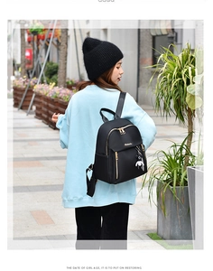 Outdoor street view of a black nylon backpack with gold zippers and panda charm