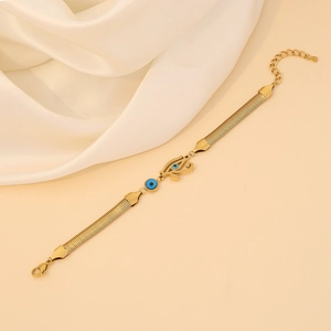 Golden snake chain bracelet featuring Horus and blue evil eye pendant on silk fabric