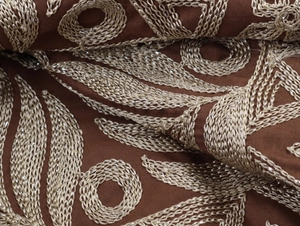 Gros plan de la broderie beige sur tissu marron avec des détails de plumes fins