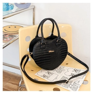Détail du sac à main noir en forme de cœur avec texture crocodile et garniture dorée sur chaise