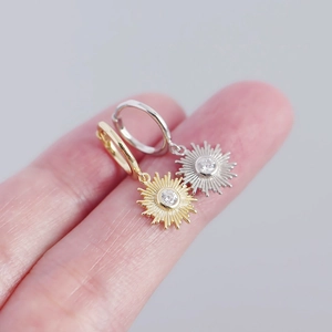 Detailed close-up of S925 silver sunburst earrings in gold and silver held by hand