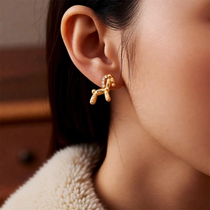 Detailed view of 18k gold balloon dog earrings with cubic zirconia on model ear