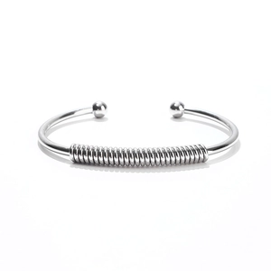 Detail of silver stainless steel open bangle featuring flexible spring coil and dual ball ends