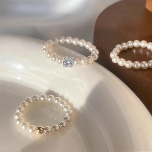 Minimalist round pearl chain rings with gold beads and square crystal accents on white ceramic